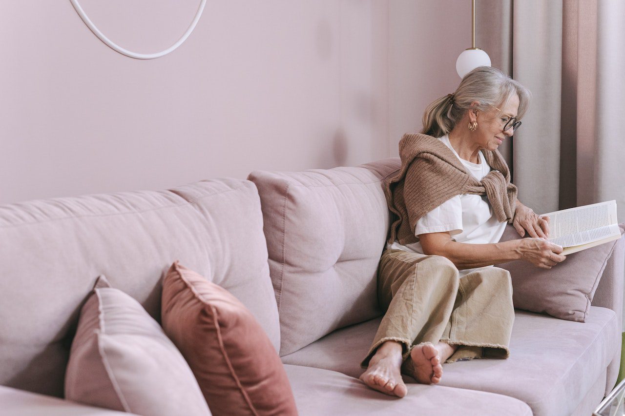 ältere Frau auf Sofa mit einem Buch