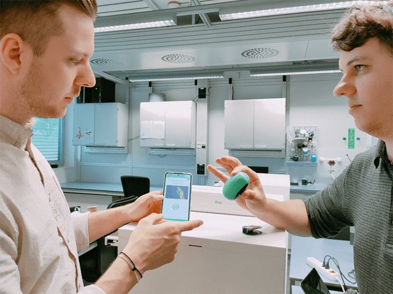 Nic Krummenacher, who can be seen on the left of the picture, holds a smartphone in his hand. The app for improving fine motor skills in Parkinson's patients is open on it. Mike Falkner can be seen on the right, holding the corresponding silicone egg with two fingers.